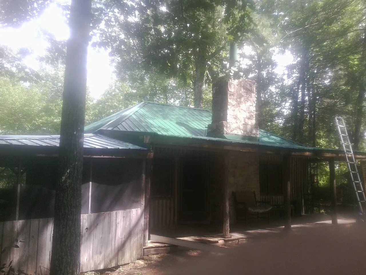 Green metal roof and stone chimney above a log cabin porch in Charlestown