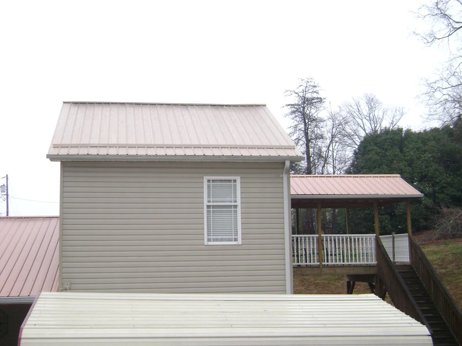 Tan metal roofs on a two story addition and attached porch, from a Roof Replacement job in Charlestown